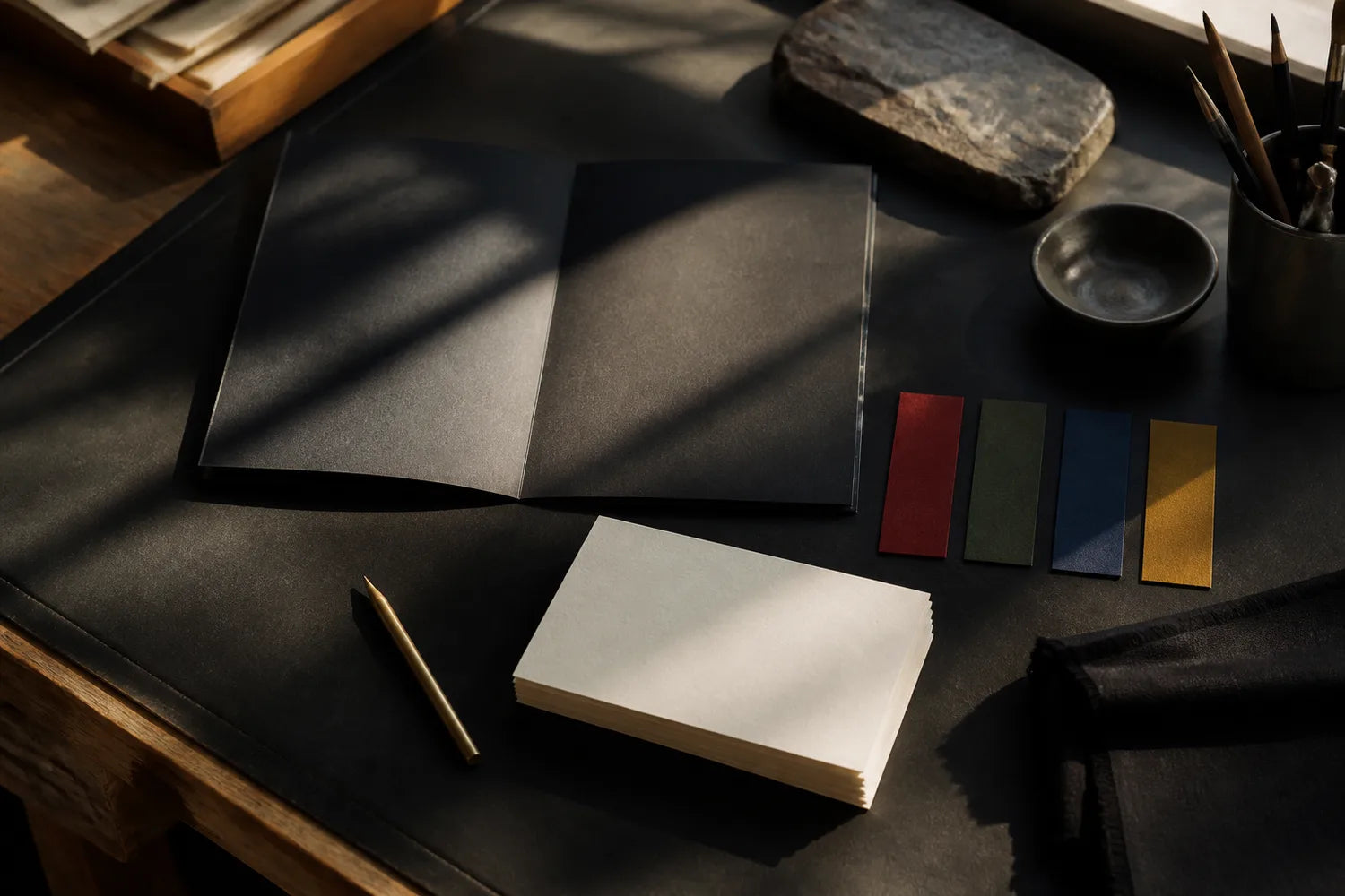 Black folio, blank cards and muted color swatches on a sunlit worktable.