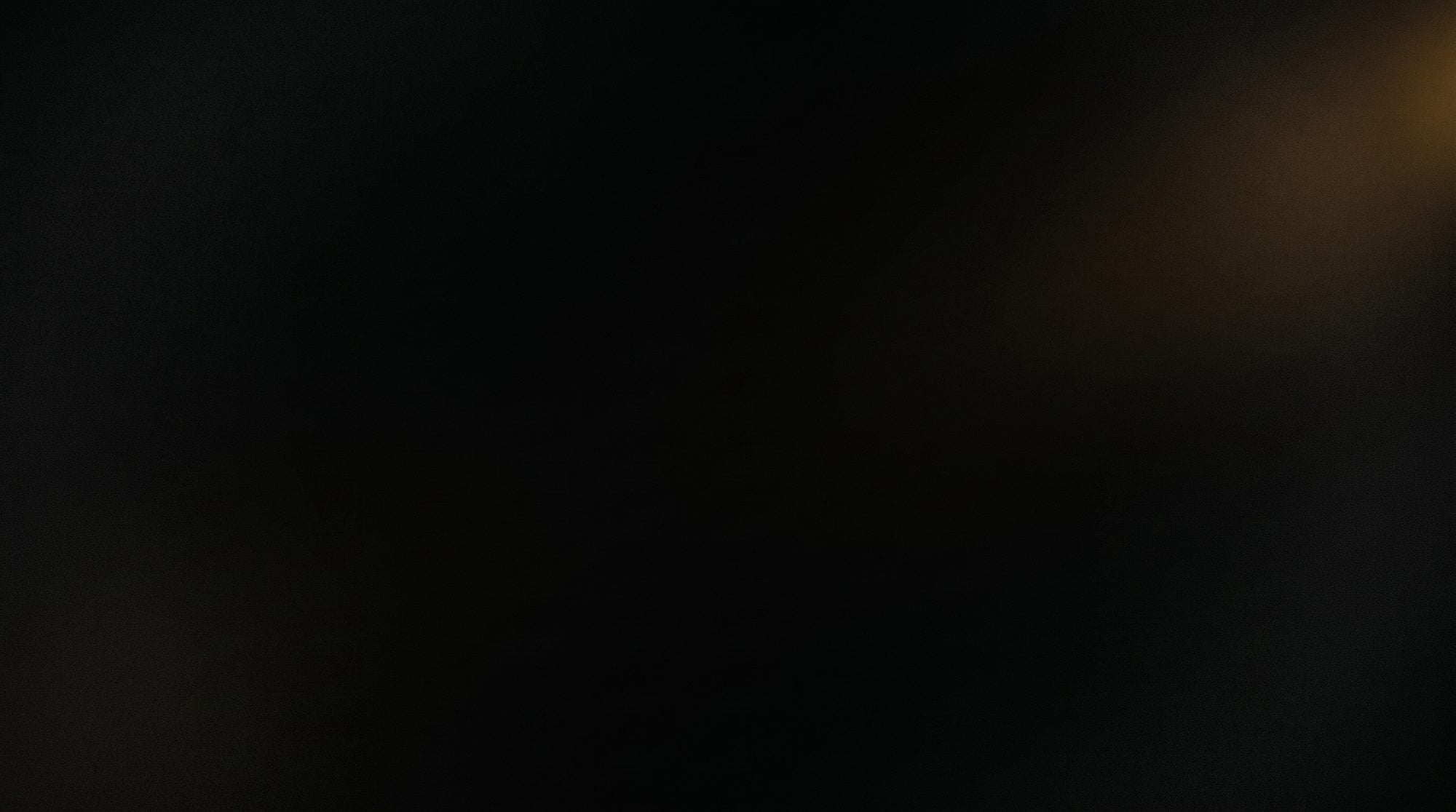 Near-black void with a faint warm amber glow in one corner
